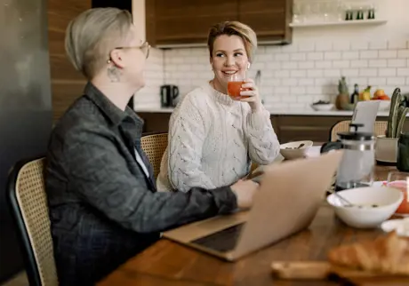 Ungt par pratar i ett kök och använder laptop