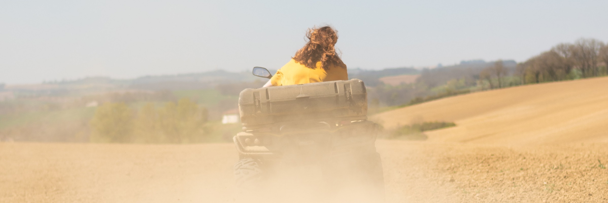 Människa på ATV åker genom dammigt fält
