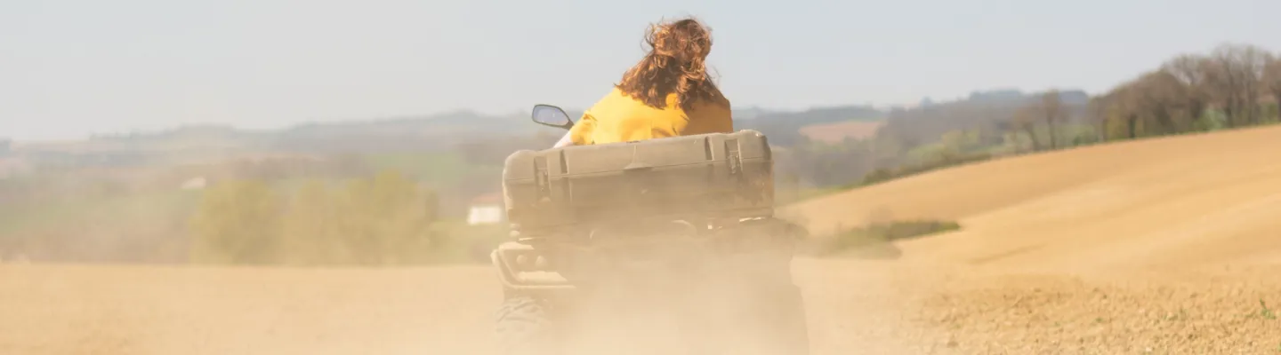 Människa på ATV åker genom dammigt fält