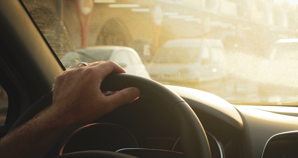 Person kör bil och håller handen på ratten i motljus