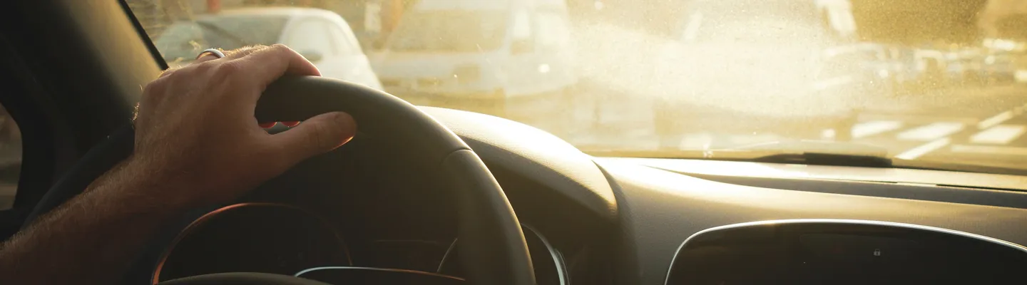 Person kör bil och håller handen på ratten i motljus