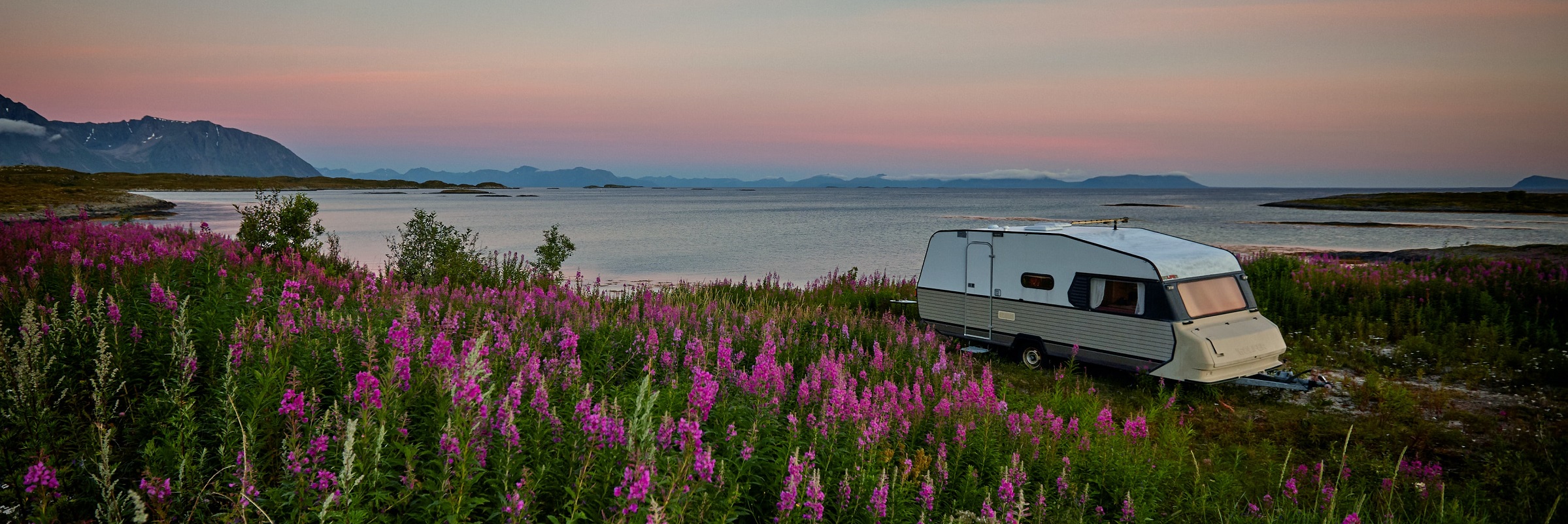 Parkerad husvagn vid fält av blommor och vatten vid kusten