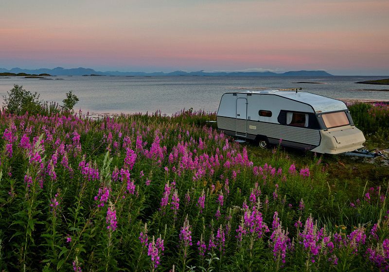 Parkerad husvagn vid fält av blommor och vatten vid kusten