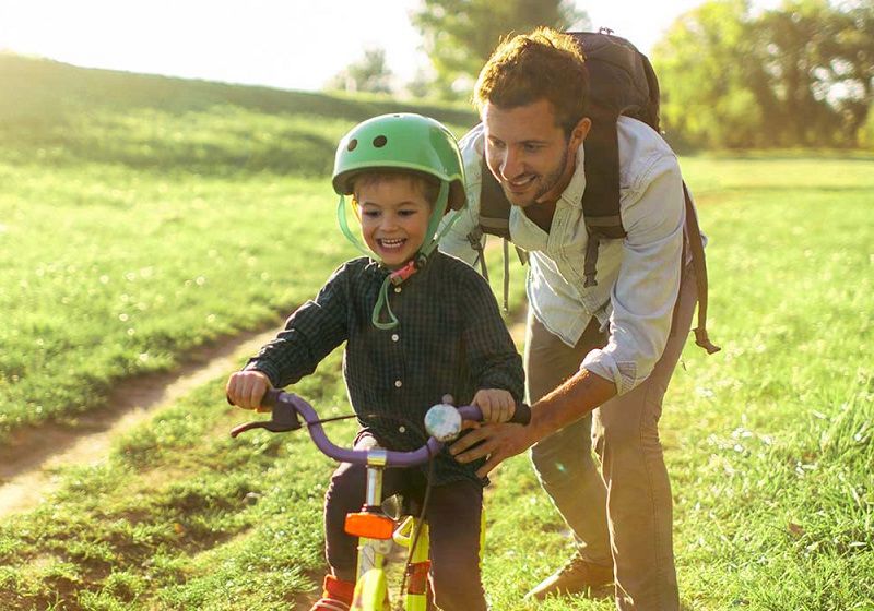 Pappa och pojke med hjälm på fält lär sig att cykla