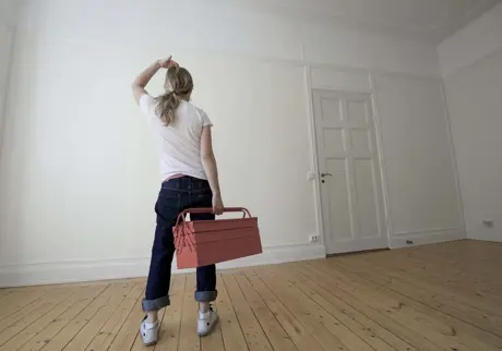 Kvinna med verktygslåda tittar på vägg