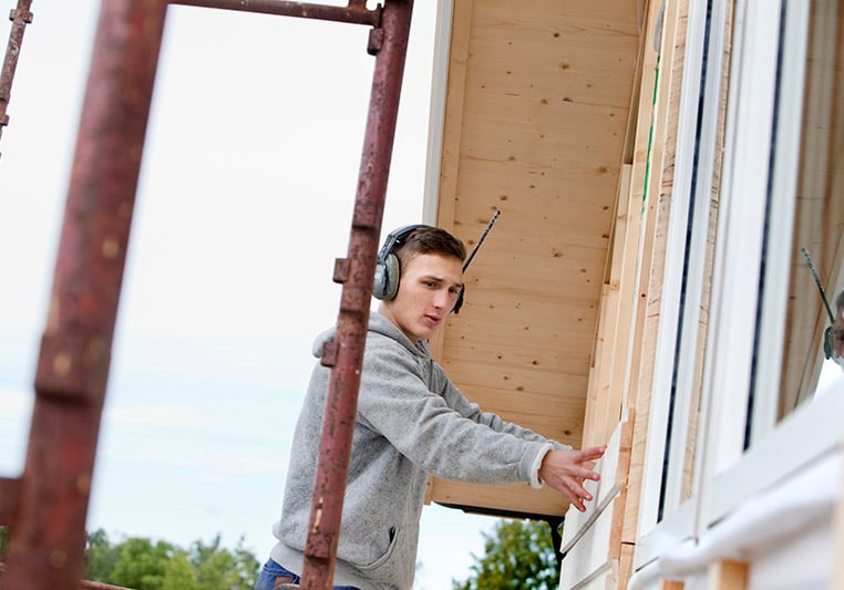 Hantverkare på byggnadsställning lägger plankor på hus