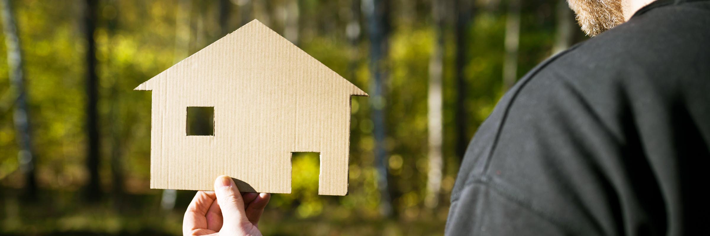 Man håller i papphus framför skogstomt