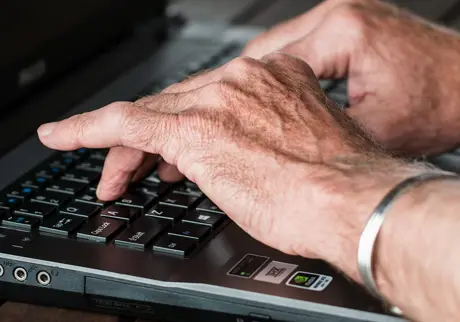 Händer på gammal man skriver på lap top