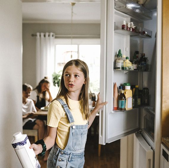 Flicka öppnar kylskåp och håller i yoghurt
