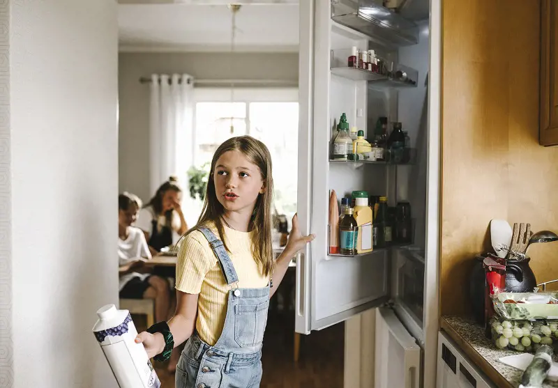 Flicka öppnar kylskåp och håller i yoghurt