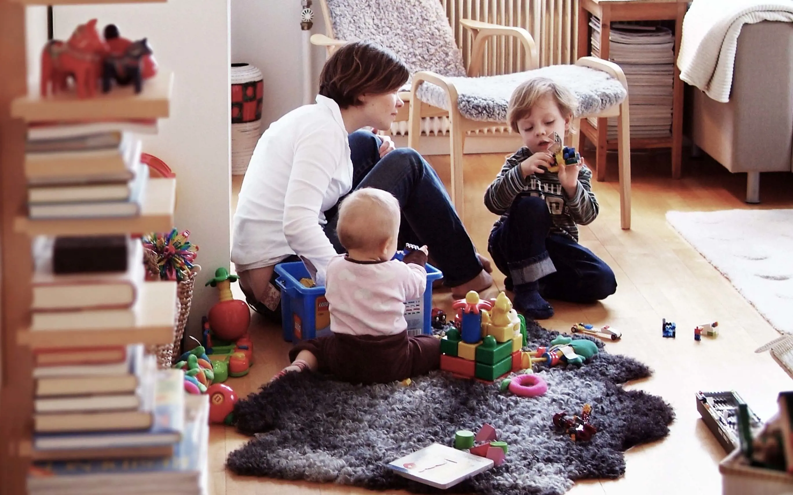 Mamma och två barn leker på matta i vardagsrum