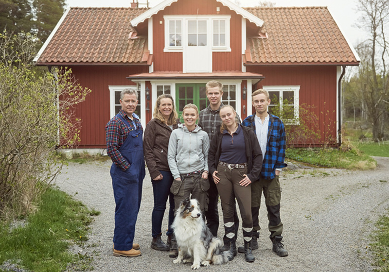 Familj med hund står utanför rött trähus