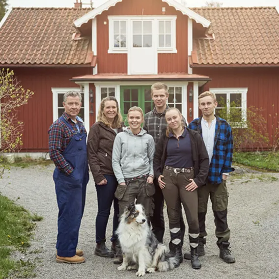 Familj med hund står utanför rött trähus