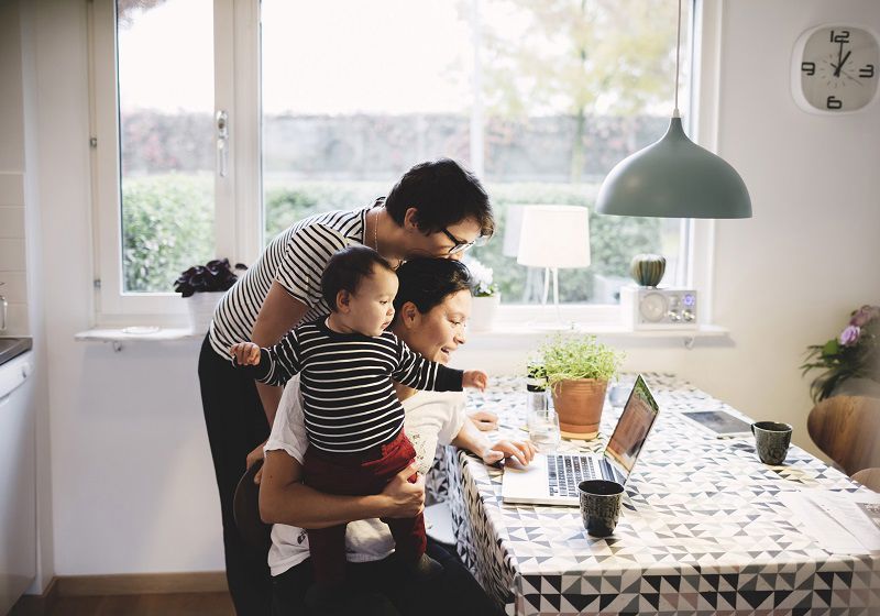 Familj i kök med spädbarn tittar på laptop