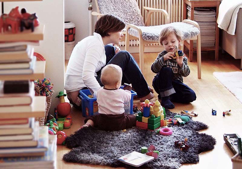 Mamma och två barn leker på matta i vardagsrum