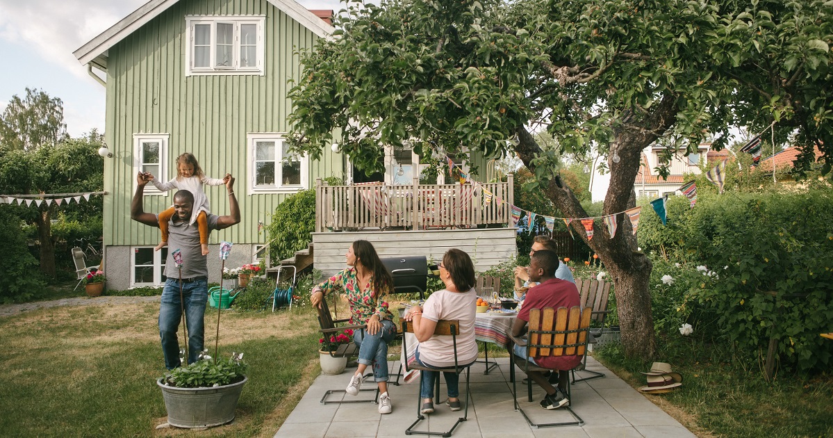 Familj i trädgården sitter i trädgårds medan dotter medan dotter sitter på pappas axlar