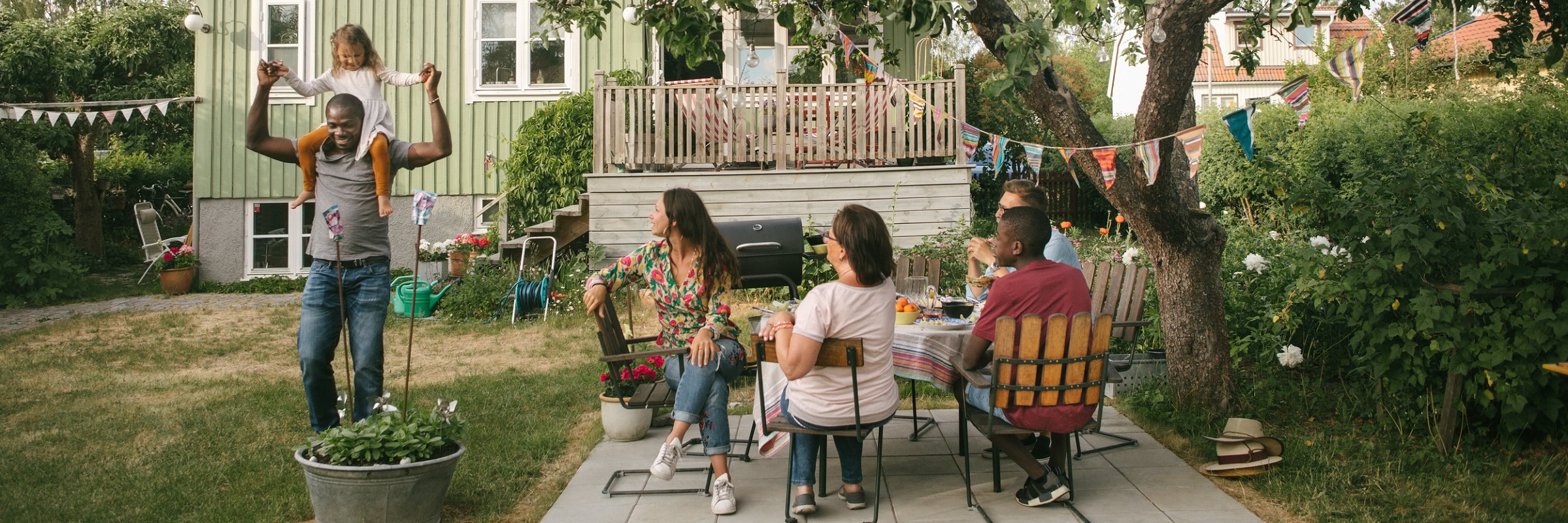 Familj i trädgården sitter i trädgårds medan dotter medan dotter sitter på pappas axlar