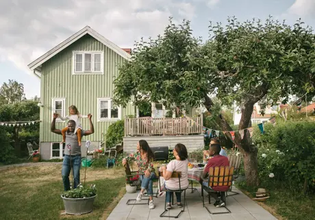 Familj i trädgården sitter i trädgårds medan dotter medan dotter sitter på pappas axlar