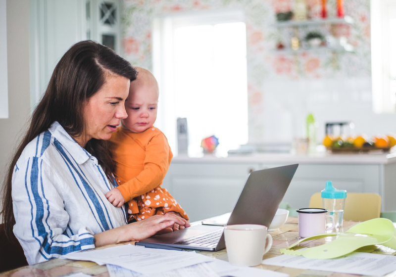 Kvinna betalar räkningar i datorn och håller en bebis