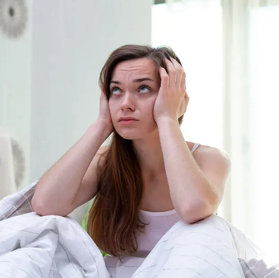 Kvinna sitter i sängen håller för öronen irriterat