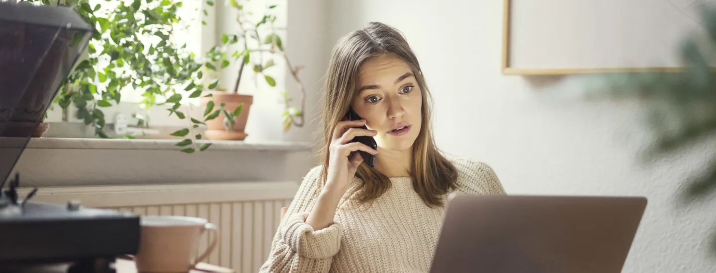 Kvinna sitter och pratar i telefon vid laptop