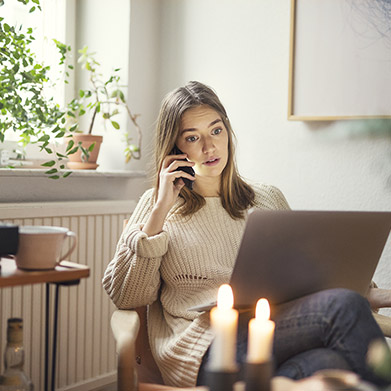 Kvinna sitter och pratar i telefon vid laptop