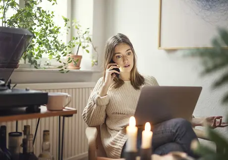 Kvinna sitter och pratar i telefon vid laptop