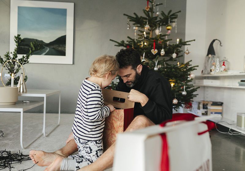 Pappa och barn öppnar julklappar framför julgran
