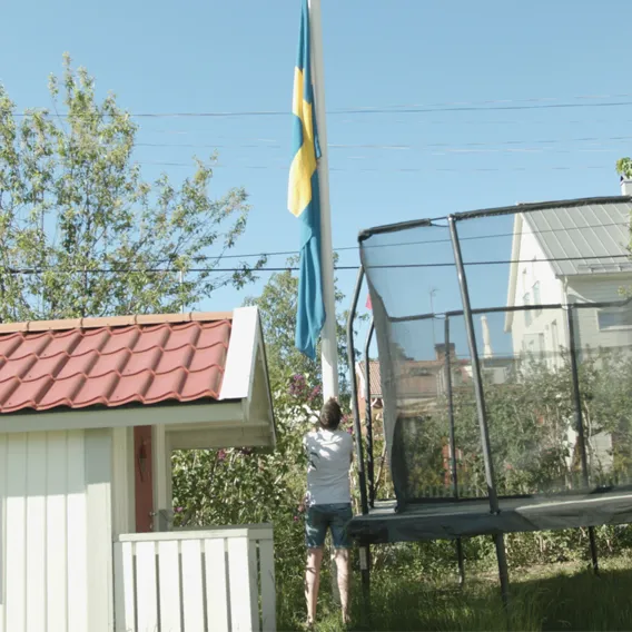 Man hissar flagga i trädgård bredvid studsmatta