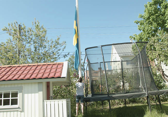Man hissar flagga i trädgård bredvid studsmatta