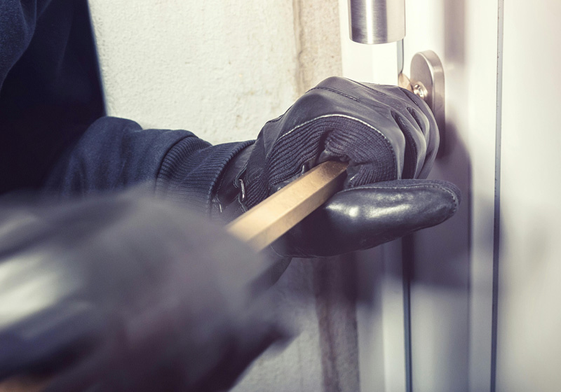 Inbrottstjuv med svarta handskar bryter upp ytterdörr med kofot