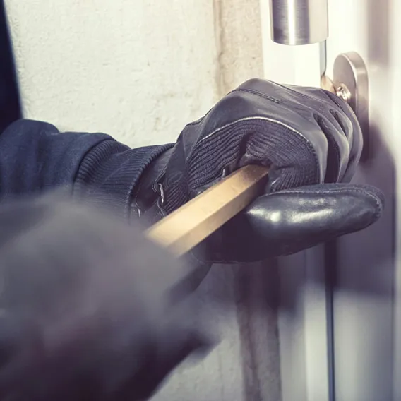Inbrottstjuv med svarta handskar bryter upp ytterdörr med kofot
