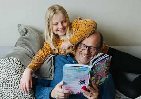 Pappa läser barnbok för dotter i grå soffa