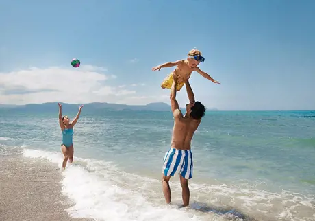 Man och två barn leker vid vattenbrynet på strand