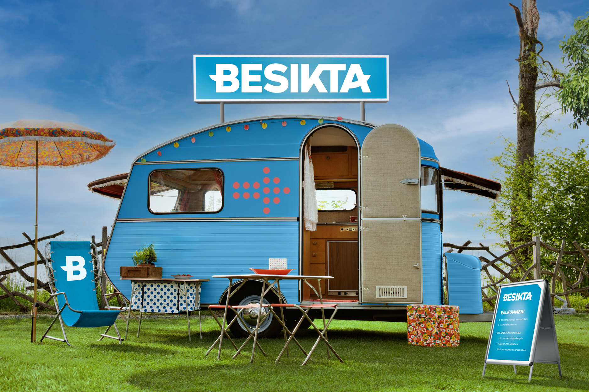 En blå liten husvagn på gräsmatta med trädgårdsmöbler utanför