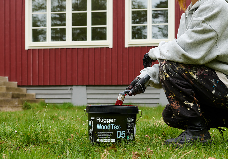 Människa som målar husfasad röd med Flügger Wood Tex 05