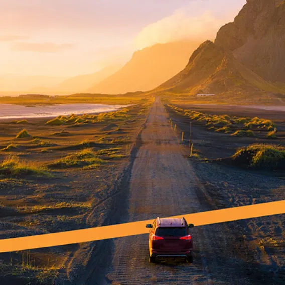 Bil på landsväg i vackert landskap i solnedgång