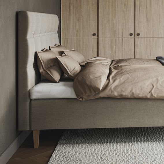 Stilrent sovrum med säng med stoppad gavel och träben, ljusbruna lakan.