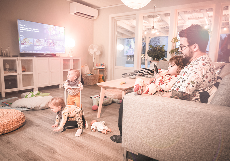 Familj, tre små barn och en pappa, leker och umgås i vardagsrum