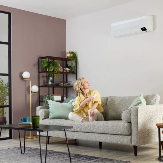 Kvinna sitter i soffa i vardagsrum och tittar upp mot en luftvärmepump på väggen